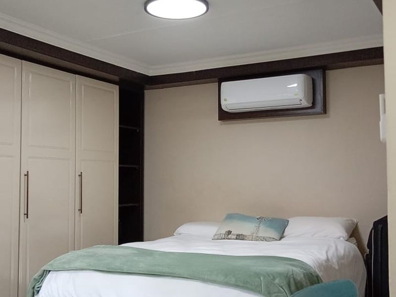A well-maintained bedroom featuring built-in cupboards, a split-system air conditioner, and modern tiled flooring with recessed ceiling lighting.