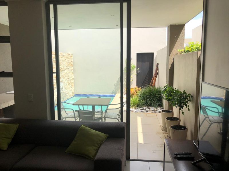 A covered patio area featuring tiled flooring and recessed lighting, seamlessly connecting to a private swimming pool and landscaped garden space.