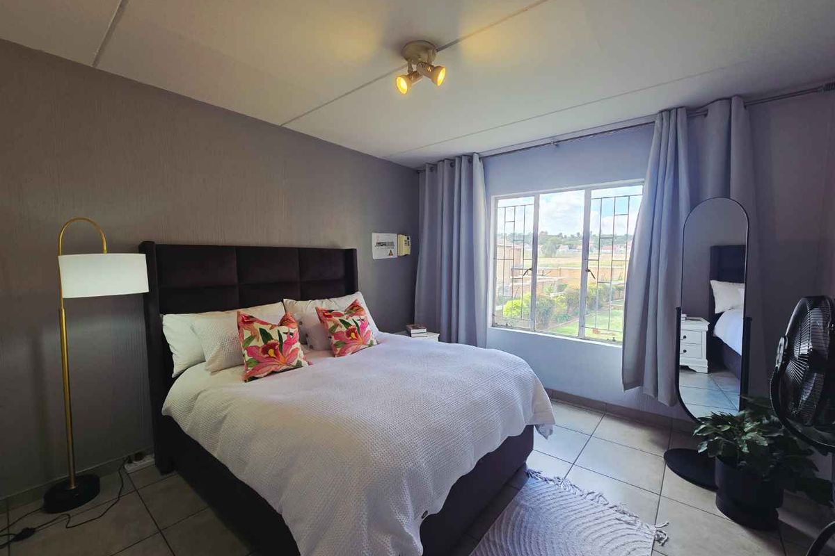 A well-lit bedroom featuring tiled flooring, a large window with security bars, and a neutral wall finish.