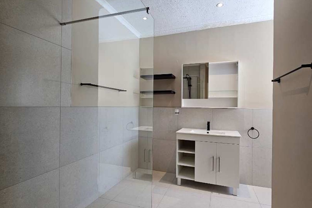 Modern bathroom featuring a spacious walk-in shower with glass screen, contemporary vanity cabinet, and neutral tiled finishes throughout.