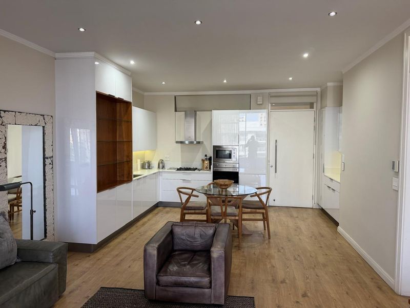 Modern open-plan living area featuring a sleek kitchen with built-in appliances, stone countertops, and high-quality laminate flooring throughout.