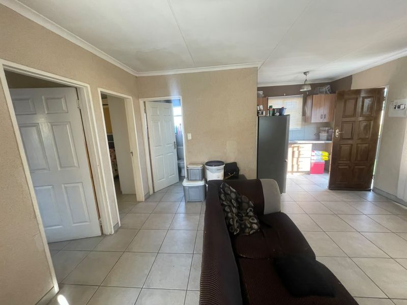 Open-plan living area featuring tiled flooring and a connected kitchen space with built-in cabinetry, requiring cosmetic updates to improve the overall aesthetic.