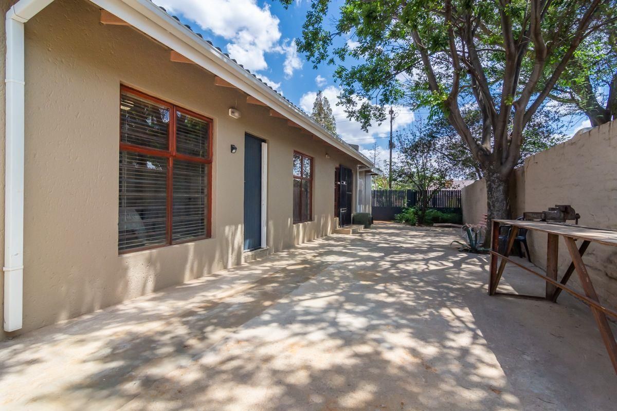 A rear exterior view of the house featuring a concrete patio area, timber-framed windows, and a perimeter boundary wall.
