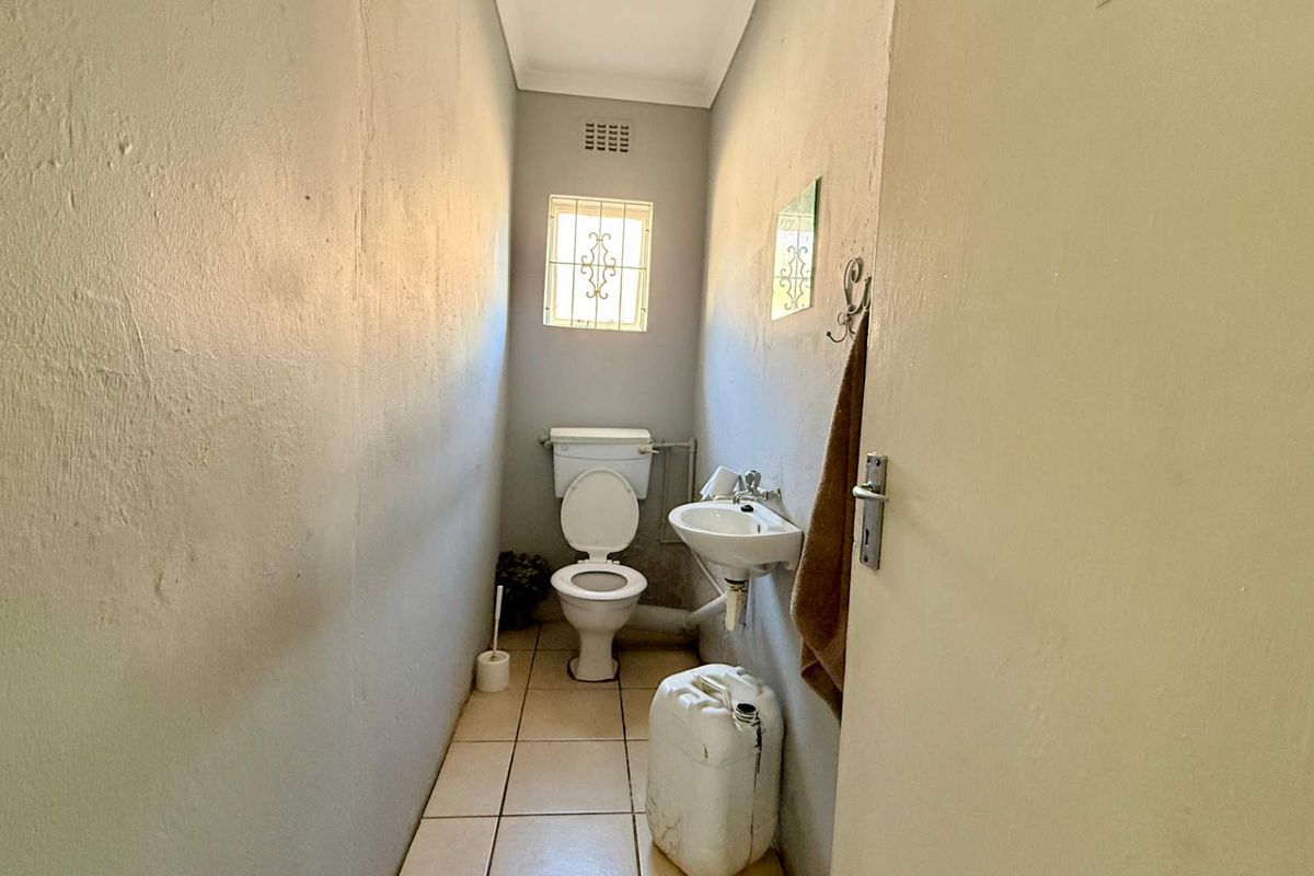 A compact, functional office restroom featuring a standard toilet, wall-mounted basin, and tiled flooring with a small security-barred window.