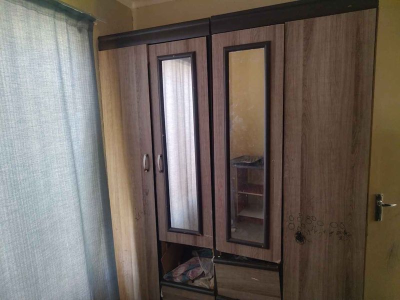 A bedroom featuring a built-in wardrobe with mirrored panels, showing signs of wear on the surrounding wall and cabinetry.