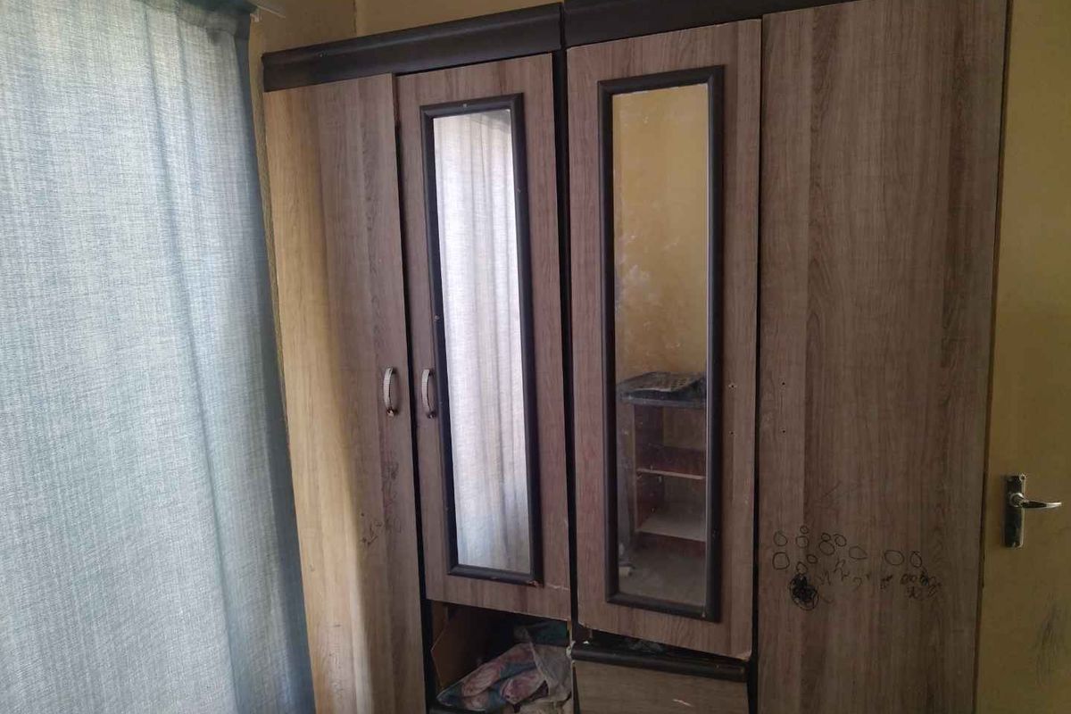 A bedroom featuring a built-in wardrobe with mirrored panels, showing signs of wear on the surrounding wall and cabinetry.