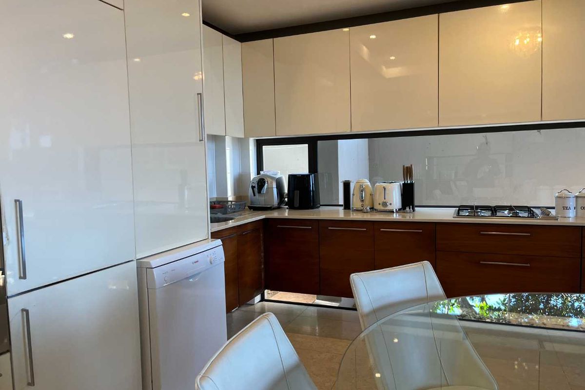 Modern kitchen featuring high-gloss white upper cabinetry, wood-finish lower cabinets, stone countertops, and a built-in gas hob.