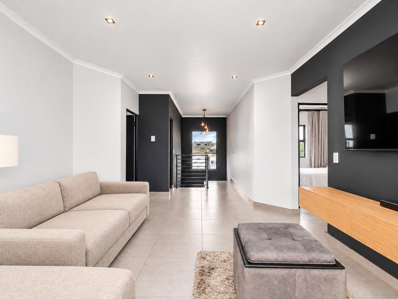 Modern open-plan living area featuring neutral tiled floors, a sleek floating media console, and contemporary dark accent walls with recessed lighting.
