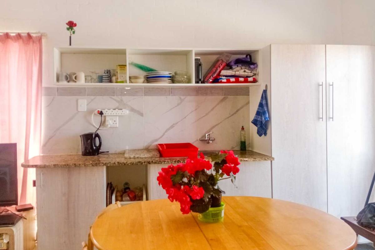 A compact kitchen area featuring granite countertops, marble-look tile backsplash, built-in cabinetry, and open shelving for storage.