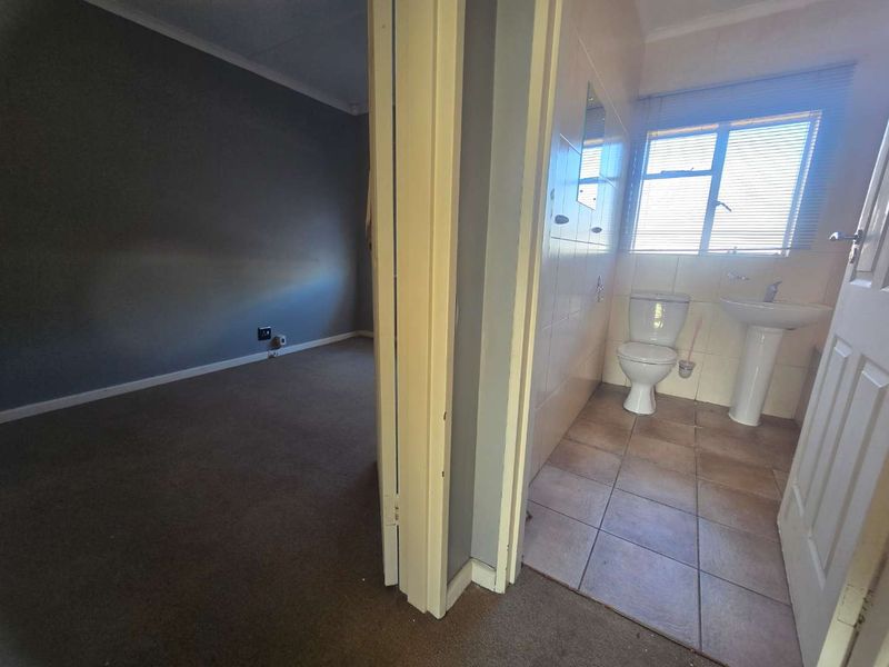 A view from a hallway looking into an empty bedroom and a functional bathroom with a pedestal basin and toilet.