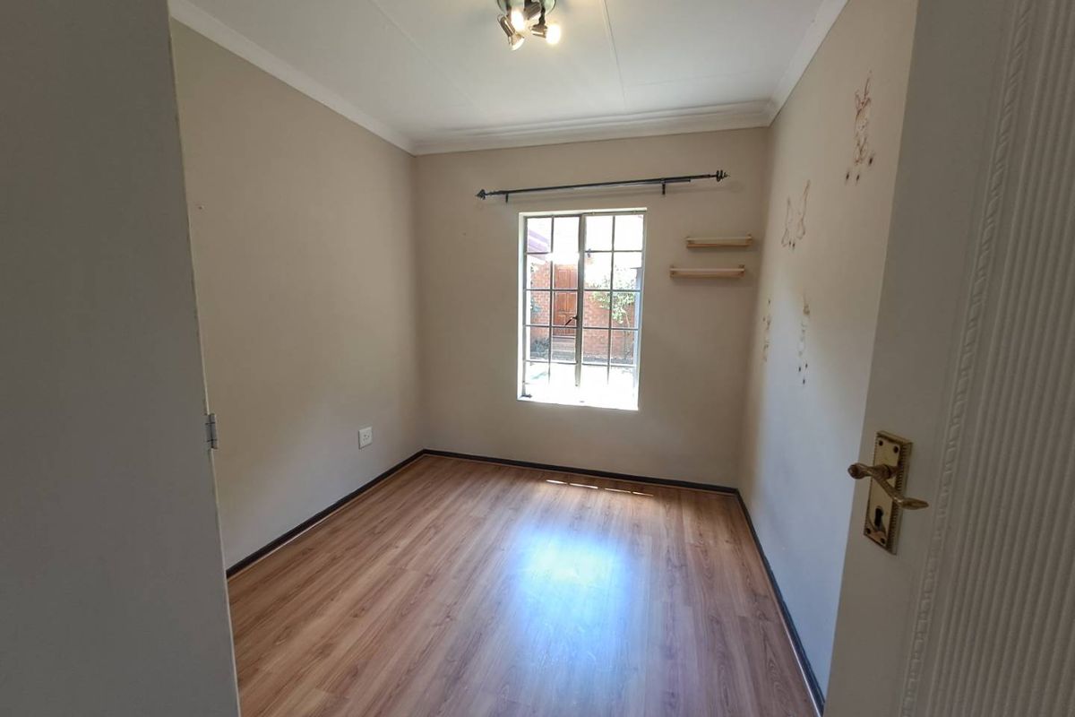 A vacant bedroom featuring laminate flooring, a window with security bars, and neutral wall finishes, offering a blank canvas for personalization.