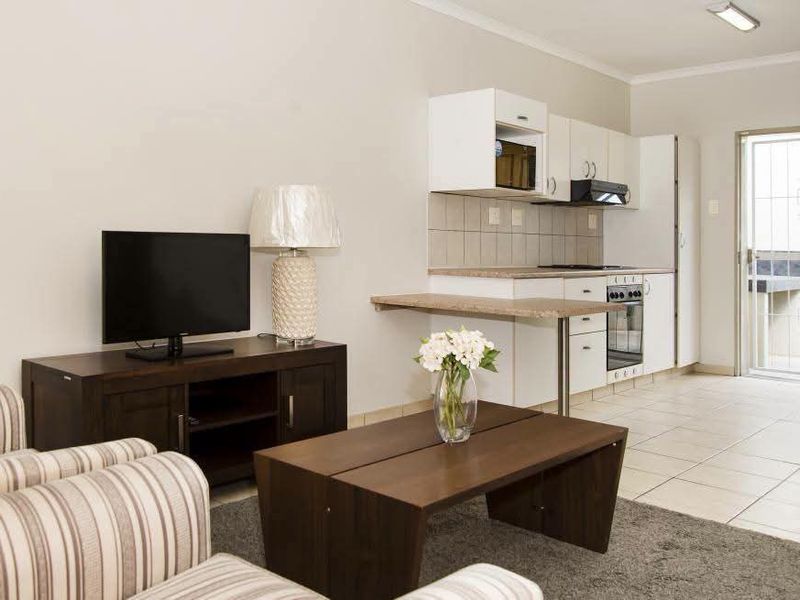 Open-plan living area featuring a compact kitchen with built-in cabinetry, oven, and extractor fan, leading to a tiled floor space with direct exterior access.