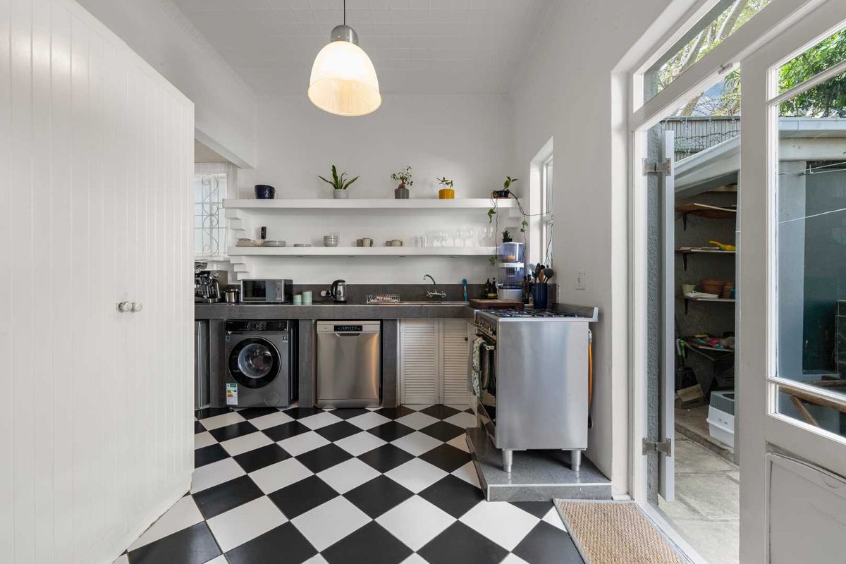 A functional kitchen featuring checkerboard flooring, open shelving, concrete countertops, and a freestanding stove, with direct access to an outdoor area.