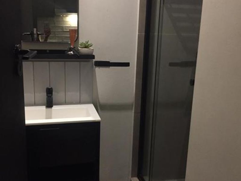 Modern bathroom featuring a sleek vanity with basin, wall-mounted mirror, and a glass-enclosed shower with contemporary black fixtures.