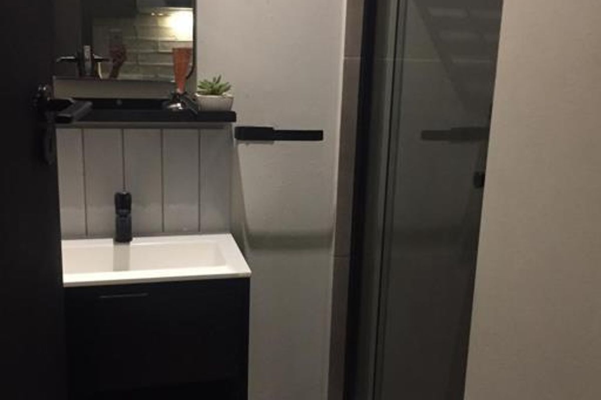 Modern bathroom featuring a sleek vanity with basin, wall-mounted mirror, and a glass-enclosed shower with contemporary black fixtures.