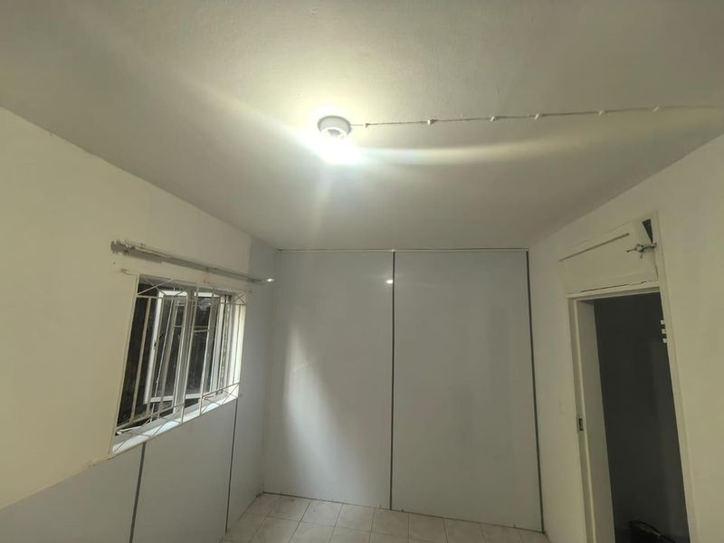 An empty bedroom featuring tiled flooring, a built-in sliding door wardrobe, and security burglar bars on the window.
