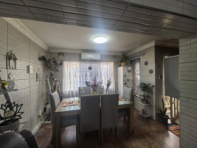 A dining room featuring brick-style wall cladding, tiled flooring, decorative ceiling molding, and a wall-mounted air conditioning unit.