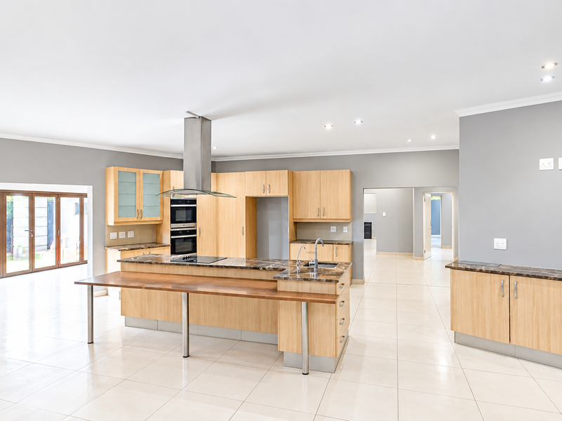 Spacious open-plan kitchen featuring light wood cabinetry, stone countertops, a central island with breakfast bar, and direct access to the outdoor patio area.