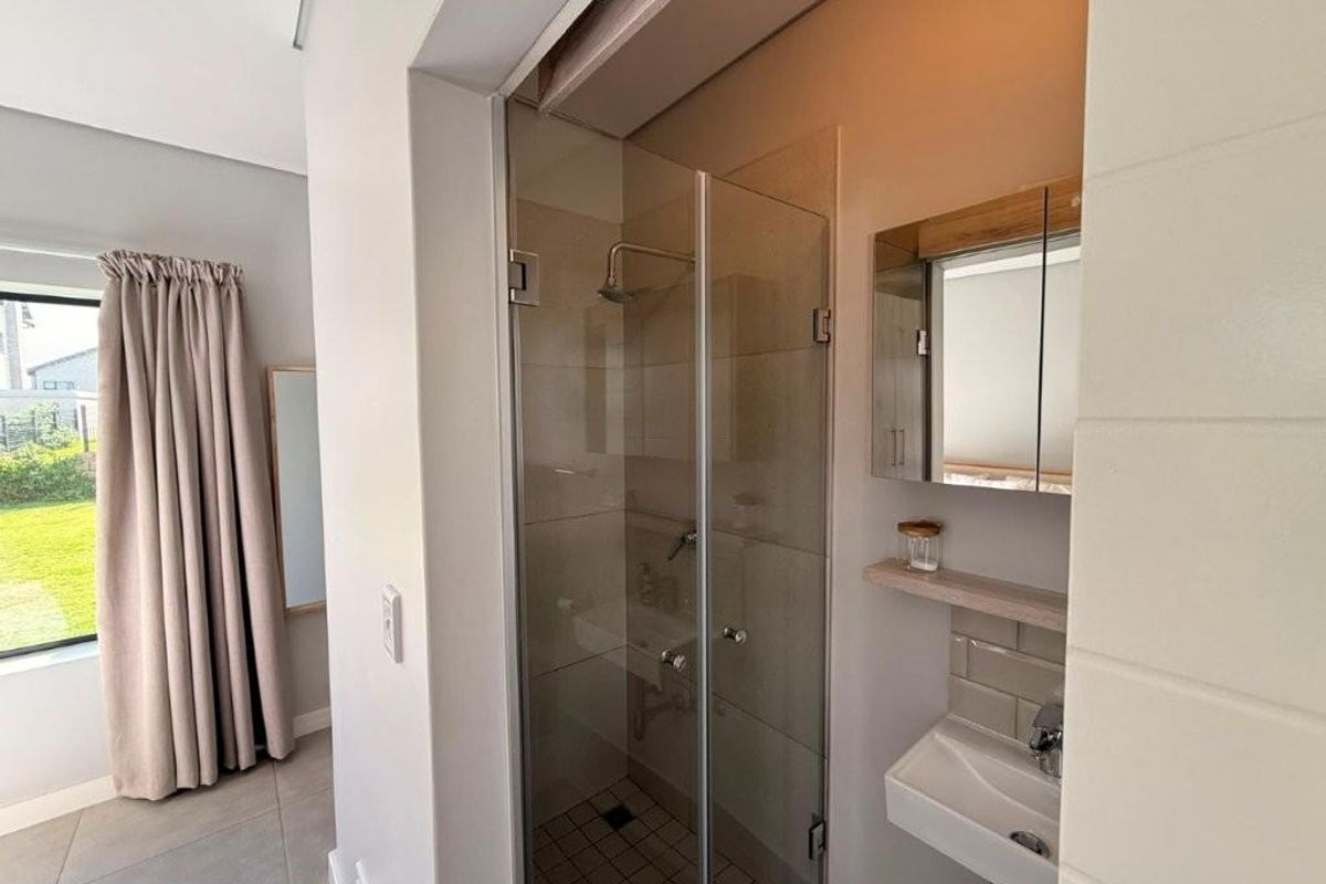 A modern en-suite bathroom featuring a glass-enclosed shower, wall-mounted basin, and mirrored cabinet, seamlessly integrated into the bedroom space.