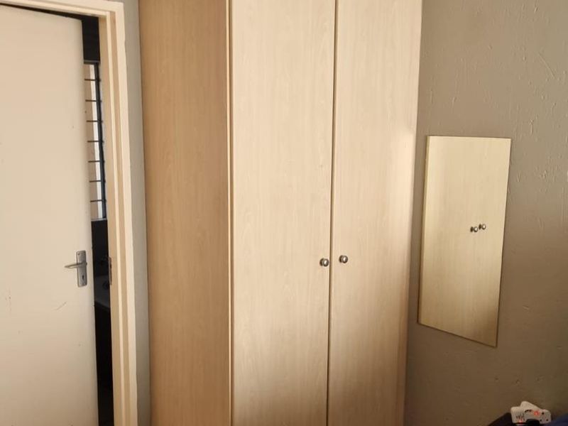 A bedroom featuring a light wood-finish built-in wardrobe and tiled flooring, with an adjacent doorway leading to another room.