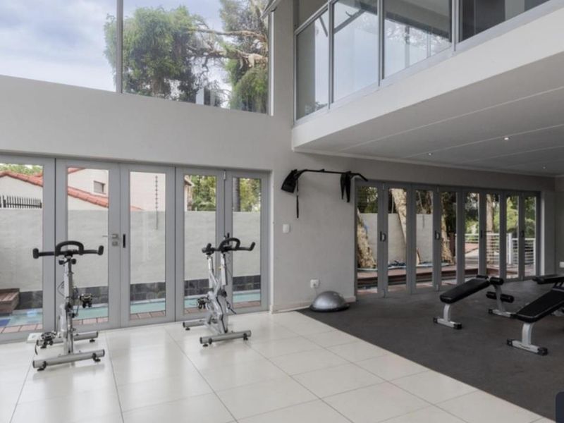 Spacious double-volume home gym featuring large glass windows, folding doors, tiled and rubber flooring, and recessed lighting with direct access to the outdoor area.