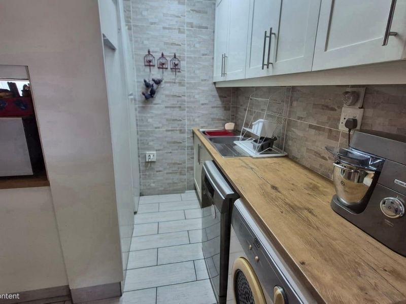 A functional scullery featuring built-in cabinetry, a stainless steel sink, timber-look countertops, and tiled finishes, providing additional workspace and utility storage.