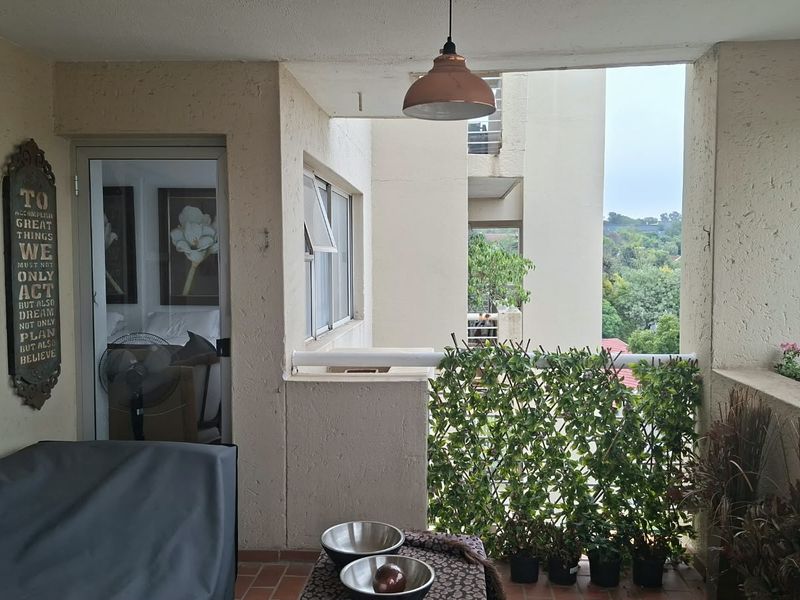 A covered balcony featuring tiled flooring, a pendant light, and built-in planter boxes, offering an outdoor space with views of the surrounding area.
