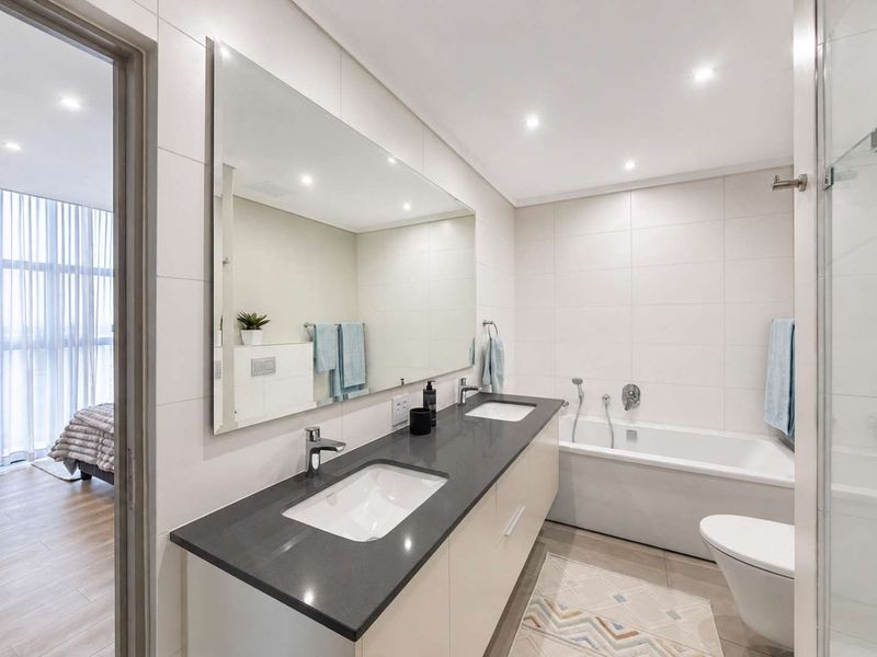 Modern bathroom featuring a double vanity with stone countertop, large wall mirror, built-in bathtub, and contemporary tiled finishes with recessed lighting.