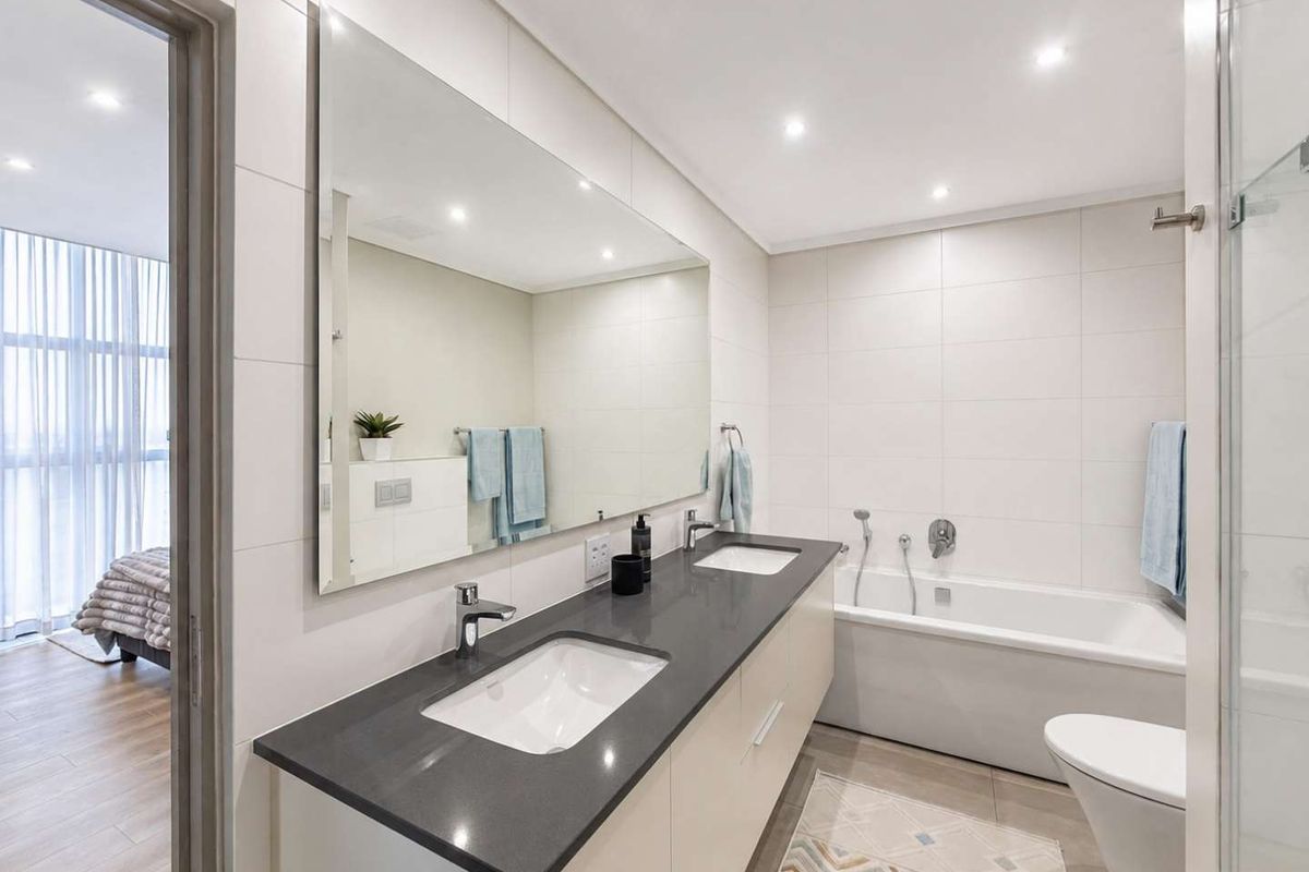 Modern bathroom featuring a double vanity with stone countertop, large wall mirror, built-in bathtub, and contemporary tiled finishes with recessed lighting.