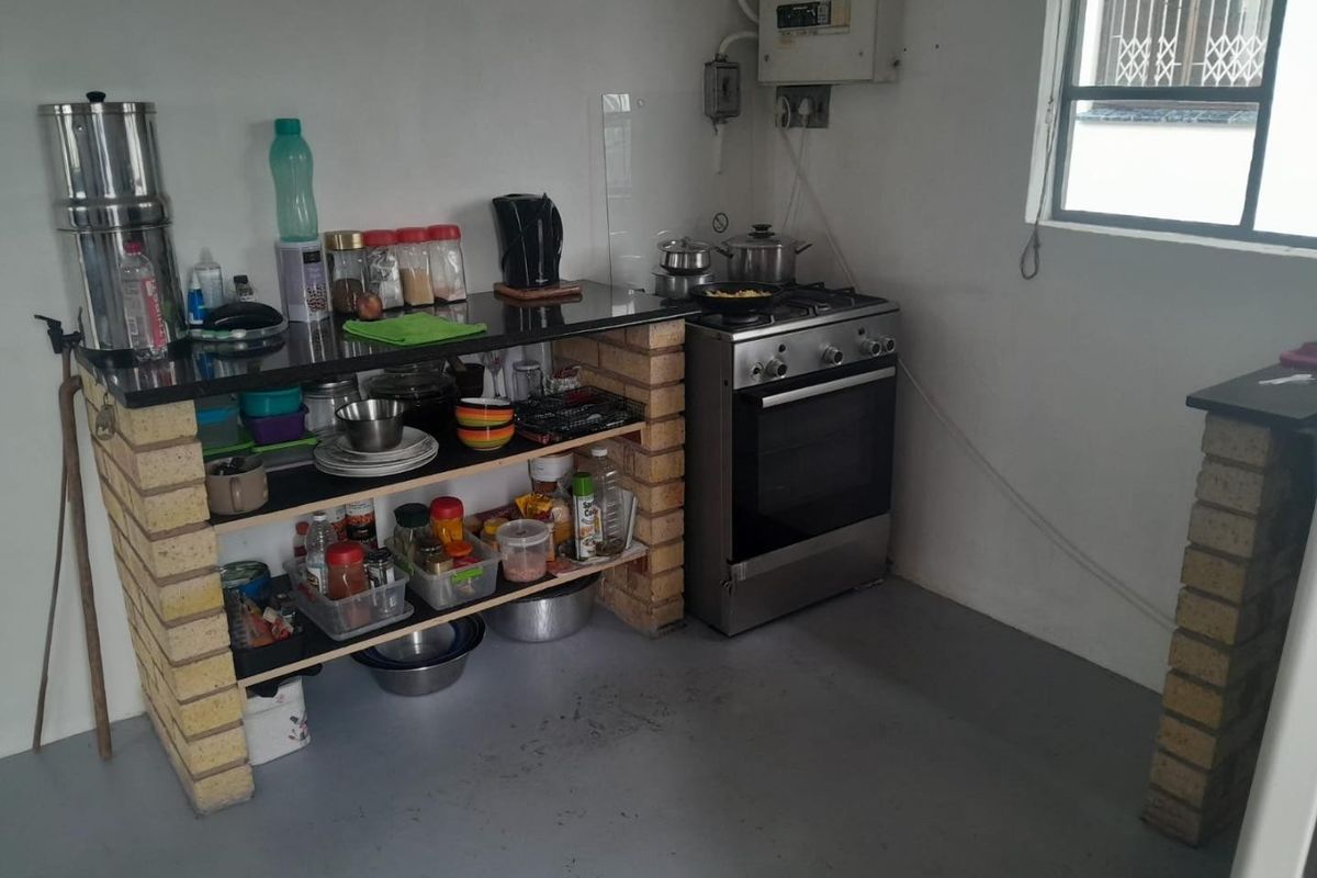 A functional kitchen area featuring a brick-based island with granite countertop, a freestanding gas stove, and exposed electrical infrastructure.