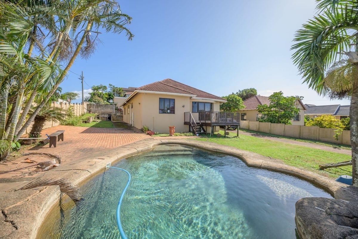Rear exterior view featuring a swimming pool, raised timber deck, paved patio area, and a well-maintained garden with perimeter walling.