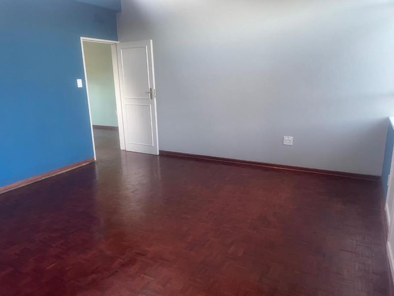 An empty bedroom featuring dark parquet flooring and a contrasting blue accent wall, providing a clean and neutral space ready for personalization.