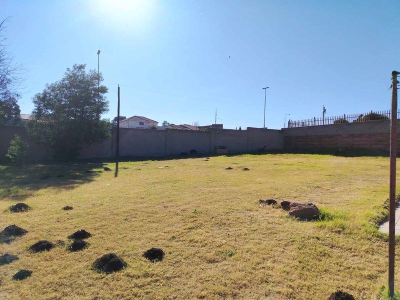 A large, open backyard area featuring a perimeter wall and metal security fencing, currently showing signs of uneven ground and soil disturbance.