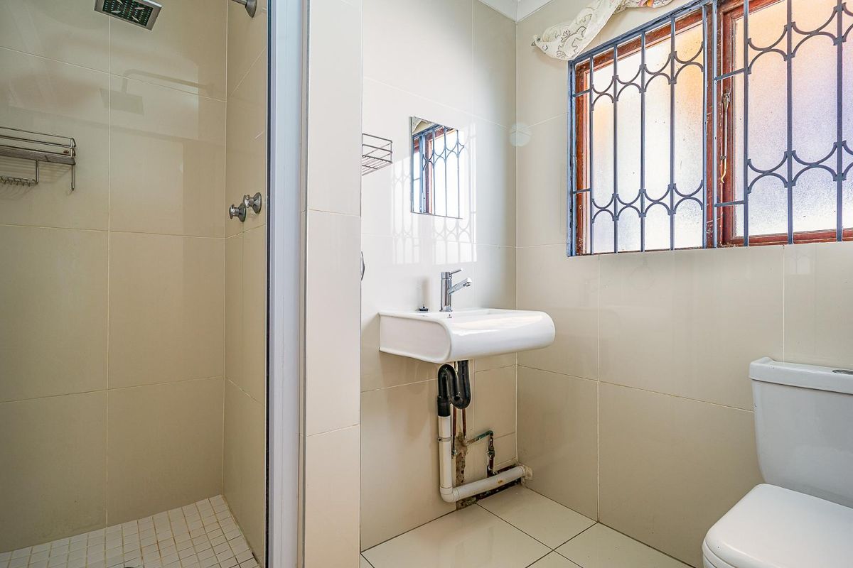 A functional bathroom featuring a shower enclosure, wall-mounted basin, and toilet, finished with neutral wall and floor tiles.