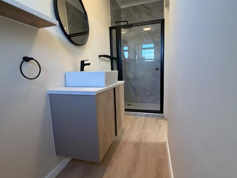 Modern bathroom featuring a floating vanity with a vessel sink, black fixtures, and a glass-enclosed shower with contemporary tiled finishes.