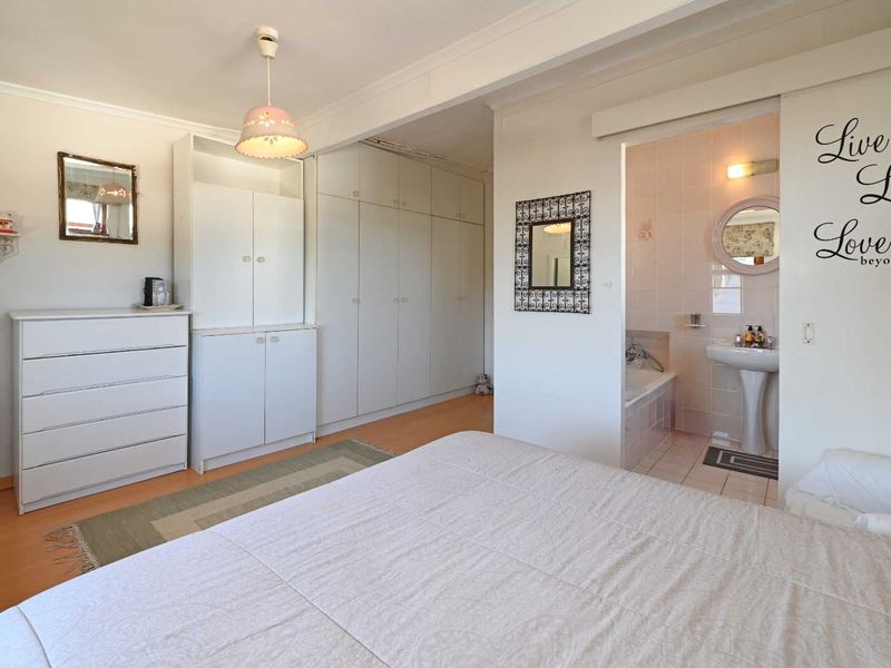 Spacious bedroom featuring extensive built-in cupboards, laminate flooring, and an open-plan en-suite bathroom with a pedestal basin and built-in bathtub.