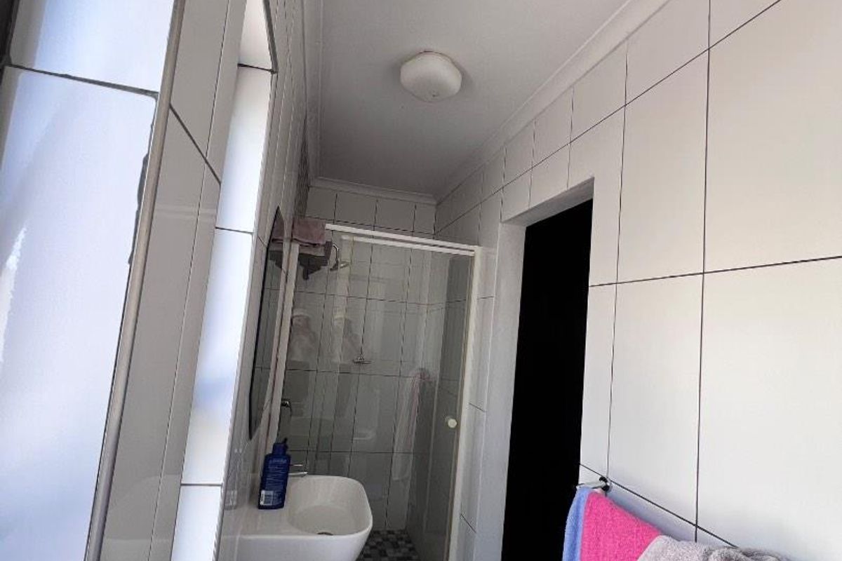 A compact bathroom featuring a wall-mounted basin, a glass-enclosed shower cubicle, and full-height wall tiling.
