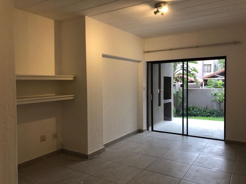 An empty living room featuring tiled floors, built-in shelving, and a sliding glass door providing access to an outdoor patio area.
