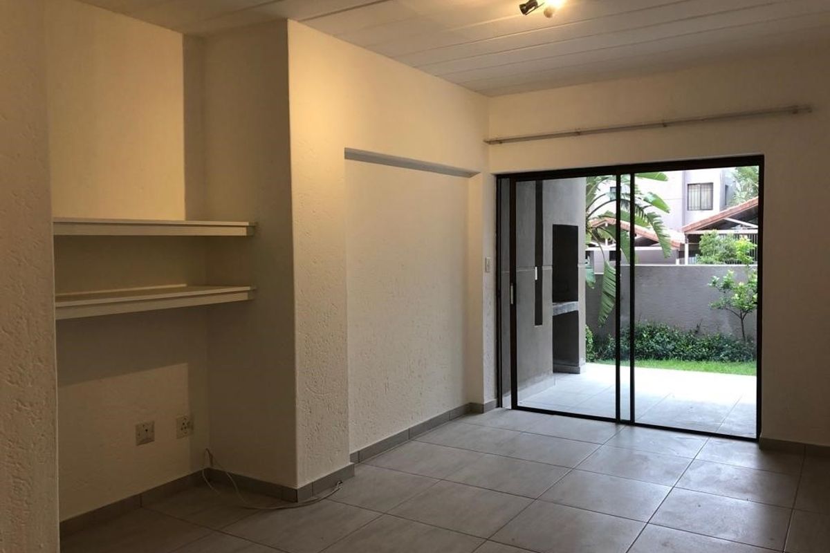 An empty living room featuring tiled floors, built-in shelving, and a sliding glass door providing access to an outdoor patio area.