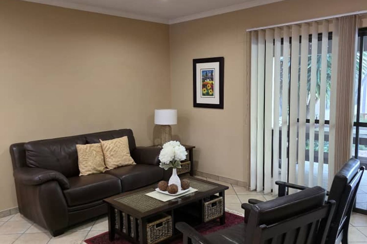 A comfortable living room featuring neutral wall tones, tiled flooring, and a sliding glass door with vertical blinds providing access to the exterior.