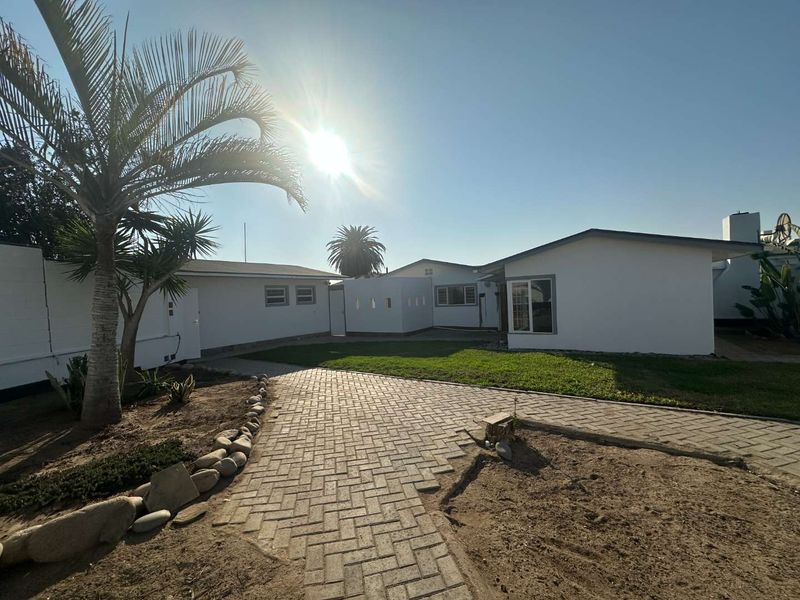 Rear exterior view of the property featuring a paved walkway, lawn area, and white painted building facade.