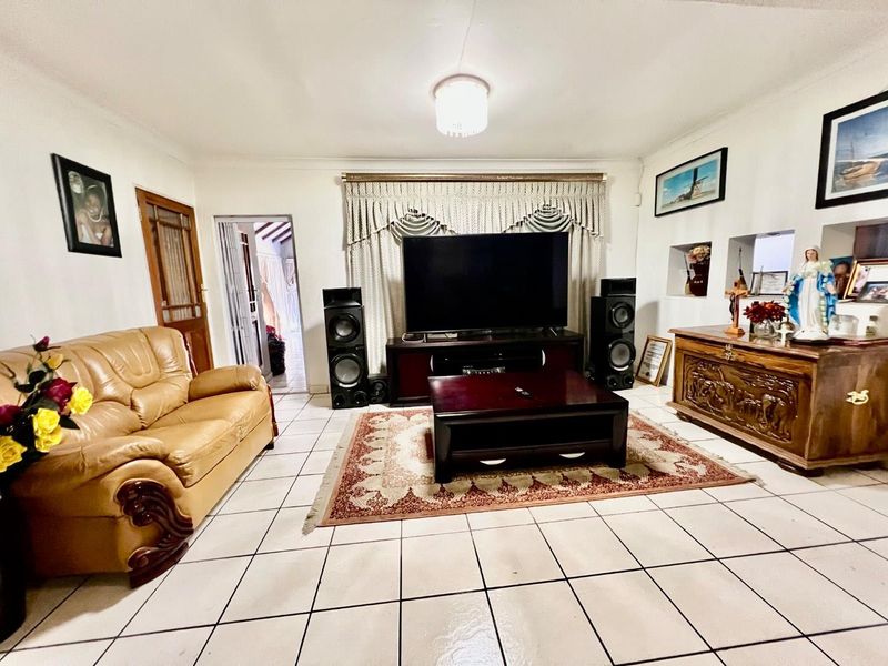 A spacious living room featuring neutral tiled flooring, coved ceilings, and a central light fixture, providing a functional and well-lit living area.