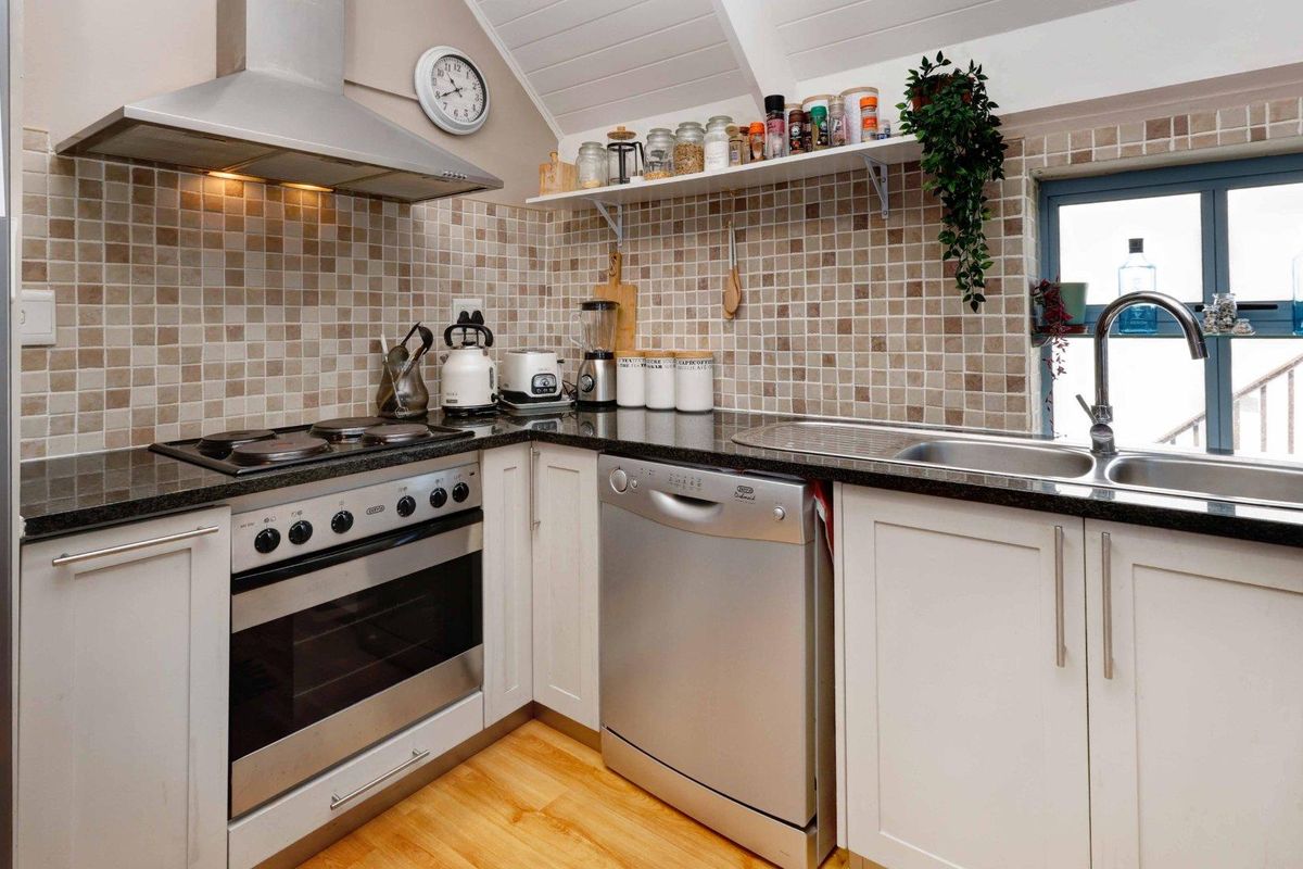 A functional kitchen featuring shaker-style cabinetry, granite countertops, a stainless steel oven with extractor fan, and a double sink with tiled splashback.