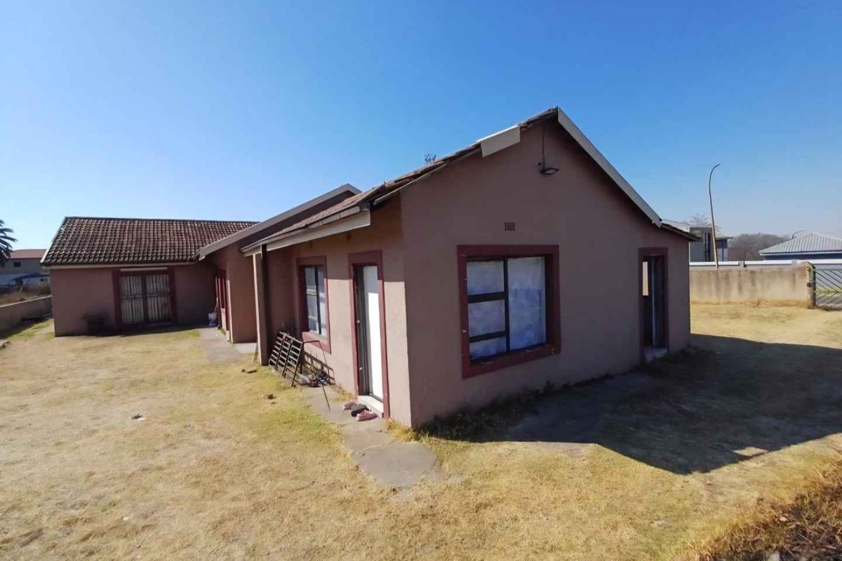 Rear view of a single-story house featuring a tiled roof, exterior masonry walls, and a surrounding yard area.