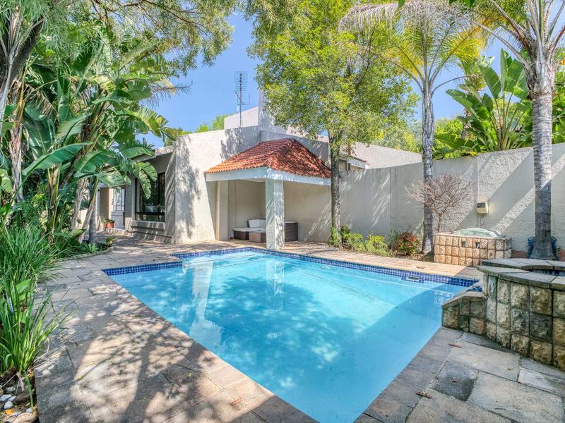 Outdoor pool area featuring a swimming pool, stone paving, and a covered patio space surrounded by established garden landscaping.