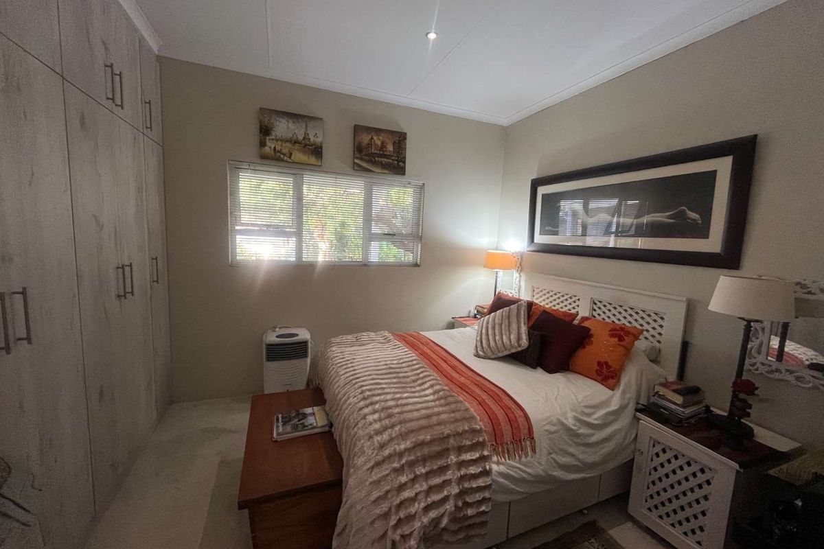 A well-maintained bedroom featuring built-in floor-to-ceiling cabinetry, neutral wall finishes, and a window with fitted blinds.