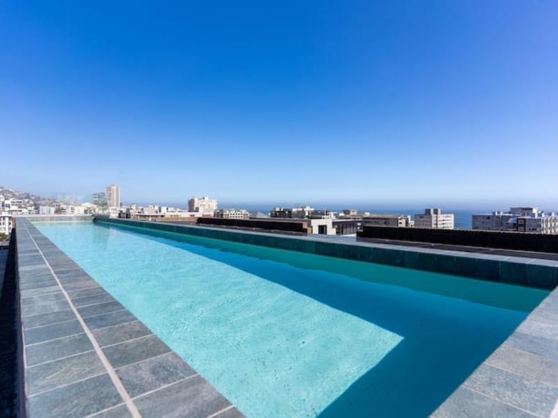 A pristine rooftop swimming pool featuring modern tiled coping and expansive panoramic city and ocean views.