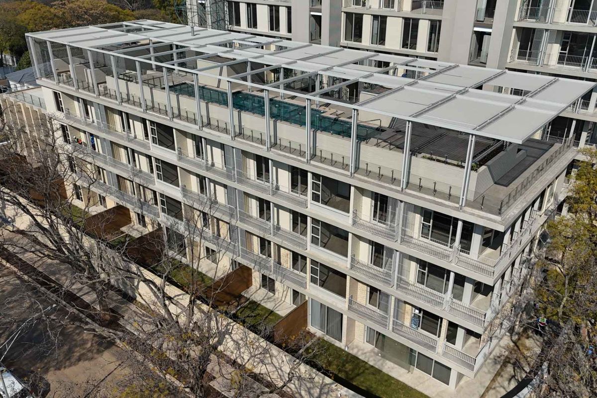 Aerial view of a modern multi-story apartment complex featuring a rooftop terrace, private balconies with glass balustrades, and landscaped ground-level areas.