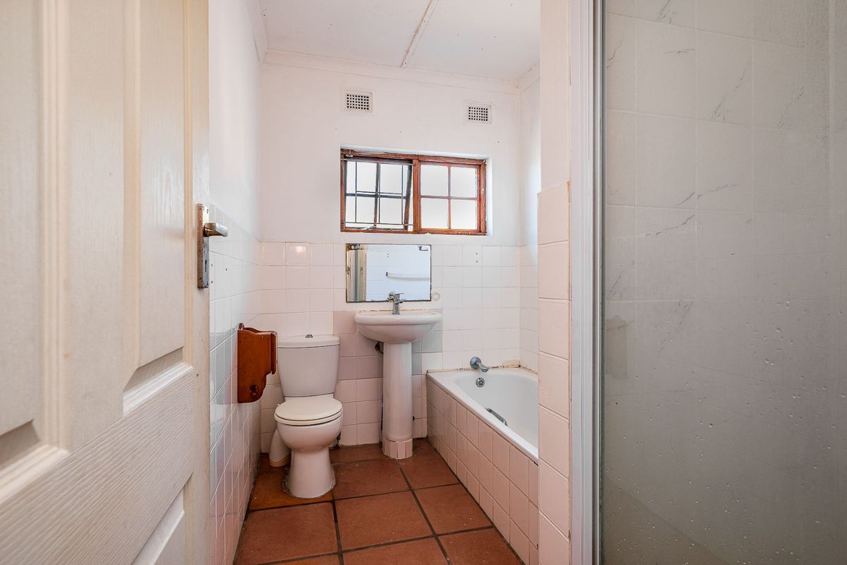 A compact bathroom featuring a pedestal basin, standard toilet, and a combined bathtub and shower unit with tiled walls and flooring.