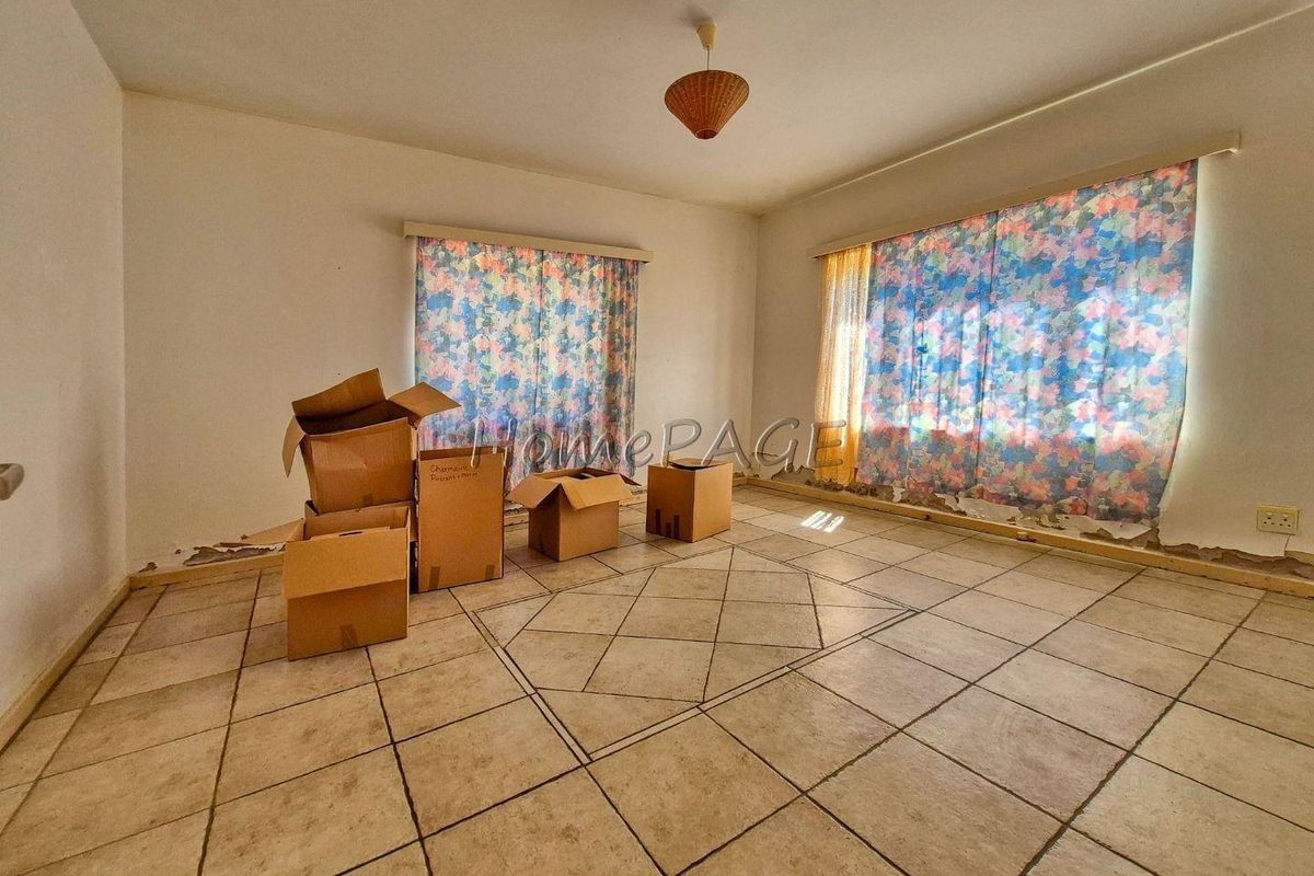 A vacant living room featuring tiled flooring and large windows, currently showing signs of wear and requiring cosmetic updates to restore its appeal.